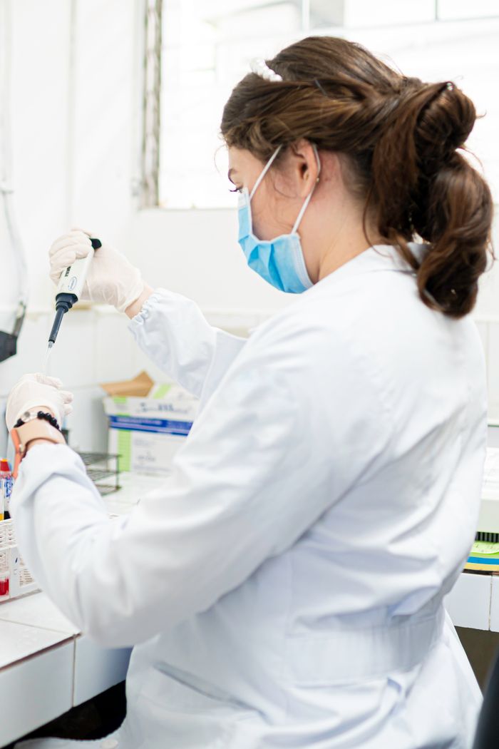 Woman scientist in lab coat performing tests with pipette in a laboratory setting.